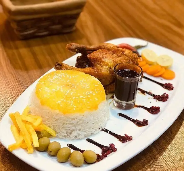 یک پرس غذای لذیذ جوجه کامل بریان با پلو زعفرانی، سیب‌زمینی سرخ‌کرده، زیتون و سس مخصوص در رستوران رزماری.