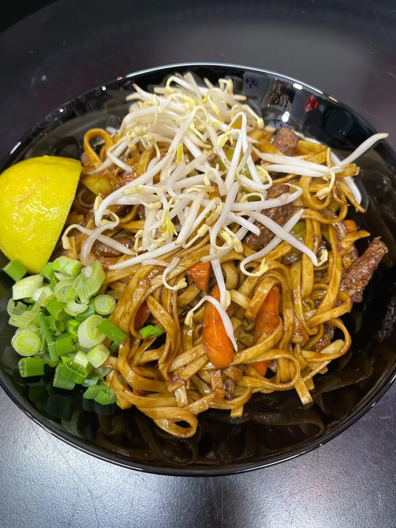 یک کاسه نودل آسیایی خوشمزه با گوشت بیف، هویج، جوانه ماش و پیازچه تازه، به همراه برش لیمو، از منوی پرطرفدار رستوران آسیایی توکیو.