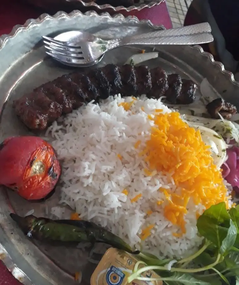 چلوکباب کوبیده لذیذ رستوران ایرانی پرسی همراه با برنج زعفرانی، گوجه کبابی، فلفل، سبزی تازه و کره، یک غذای سنتی و خوشمزه.
