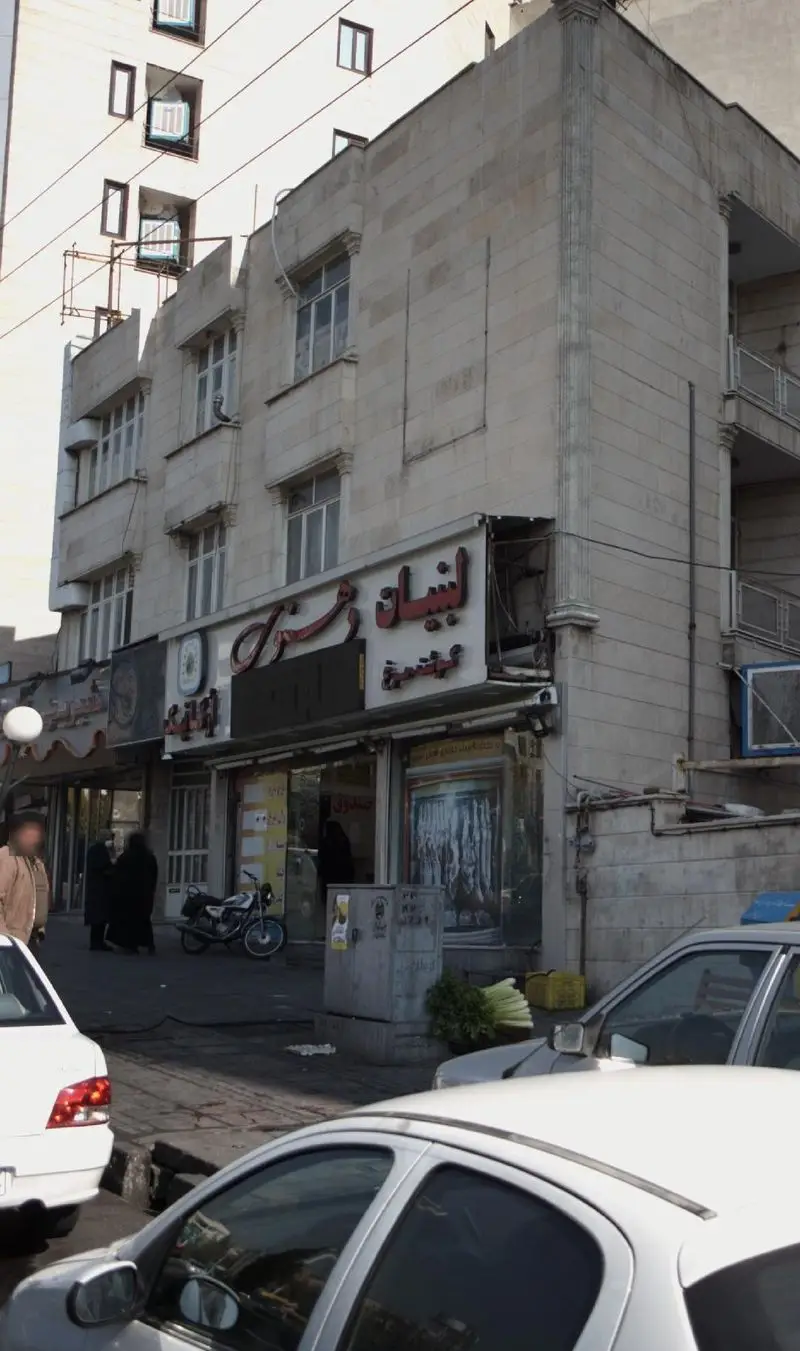 تصویر نمای بیرونی مغازه لبنیات دهنوی در خیابان، با تابلوی بزرگ فارسی، حضور مردم و خودروها. فروشگاه عرضه کننده انواع محصولات لبنی تازه و محلی با کیفیت عالی.