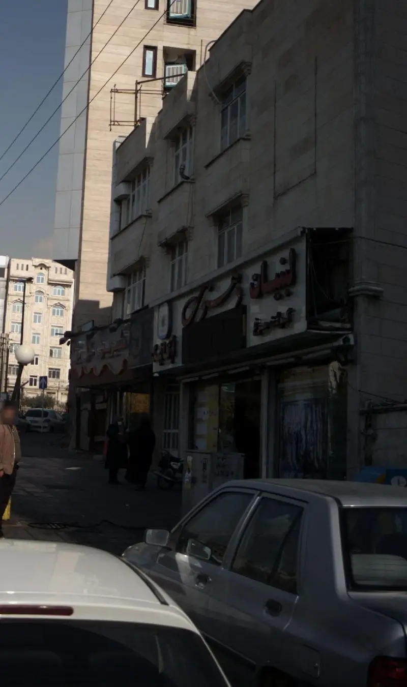 نمای بیرونی فروشگاه لبنیات دهنوی در یک خیابان شهری شلوغ با اتومبیل‌ها و عابران پیاده، نشان‌دهنده دسترسی آسان.