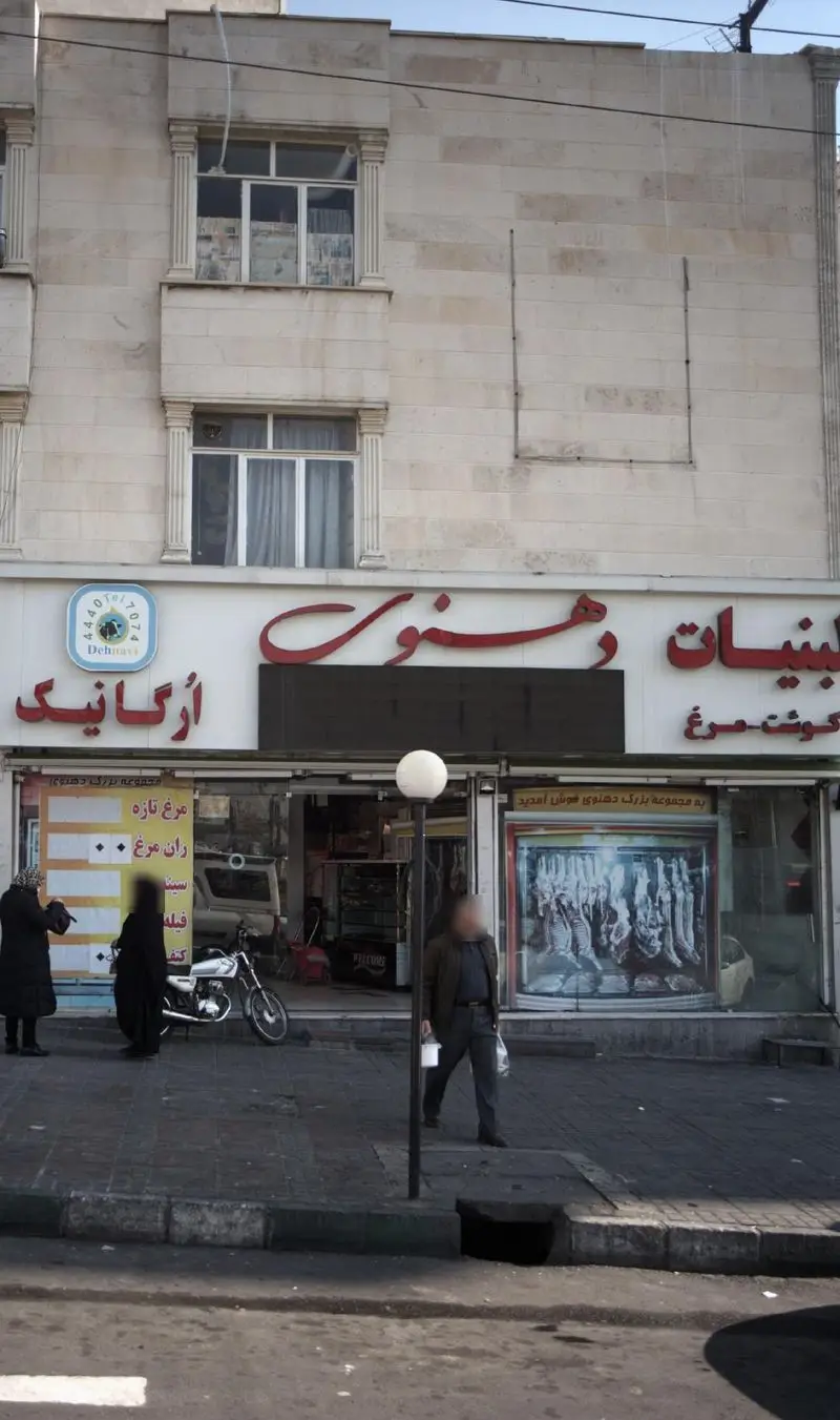 نمای بیرونی فروشگاه لبنیات دهنوی، عرضه کننده مرغ ارگانیک و گوشت تازه. تابلوی بزرگ و نمای شیشه‌ای در خیابان شهری.