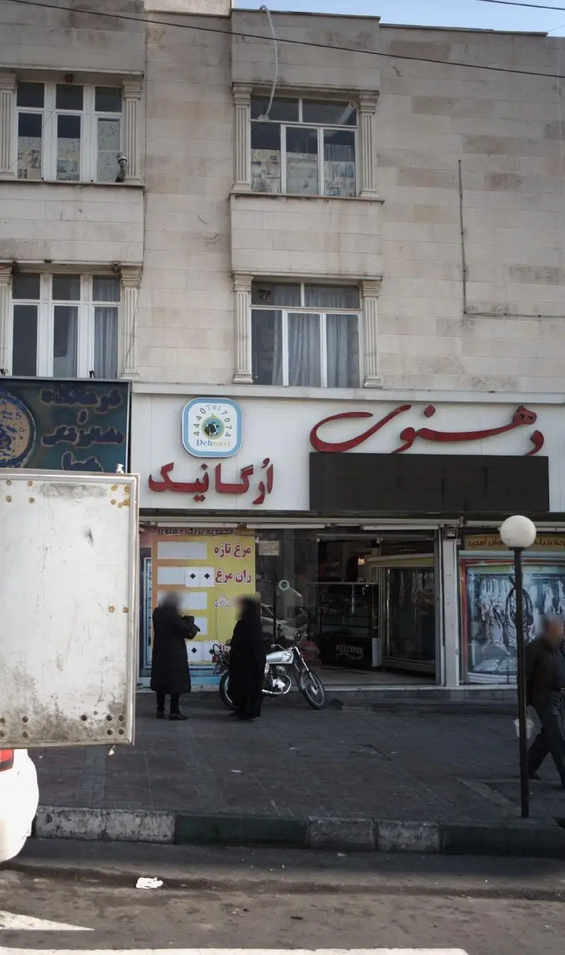 تصویری از نمای خارجی فروشگاه لبنیات دهنوی و محصولات ارگانیک در خیابان، با تابلوی روشن و مشتریانی که در پیاده‌رو ایستاده‌اند.