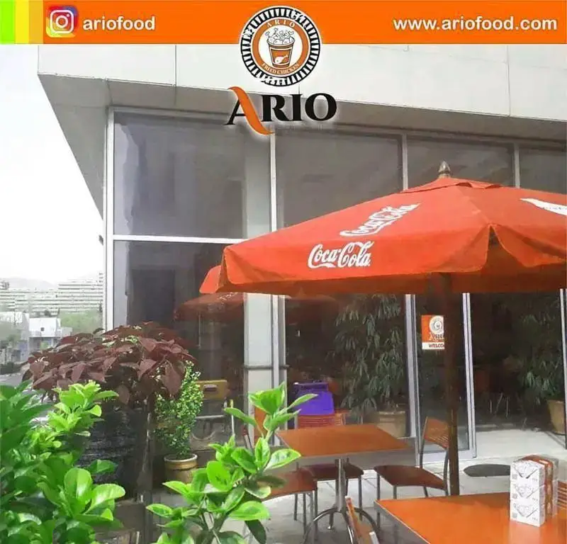 فست فود آریو، نمایی از رستوران با فضای باز، میز و صندلی، چترهای نارنجی کوکاکولا. لوگو و نام برند آریو به وضوح دیده می شود.
