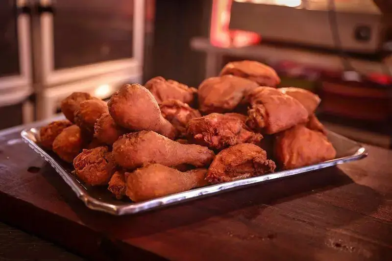 سینی بزرگ پر از تکه‌های مرغ سوخاری طلایی و خوشرنگ، مناسب برای سفارش در فست فود آریو. این غذای آماده لذیذ روی میز چوبی قهوه‌ای قرار دارد.