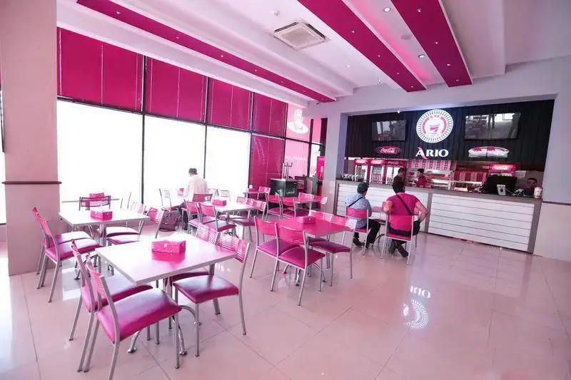 نمایی از سالن غذاخوری فست فود آریو با طراحی داخلی چشم‌نواز و صورتی رنگ، شامل میز و صندلی‌های راحت و فضایی دلنشین برای مشتریان.