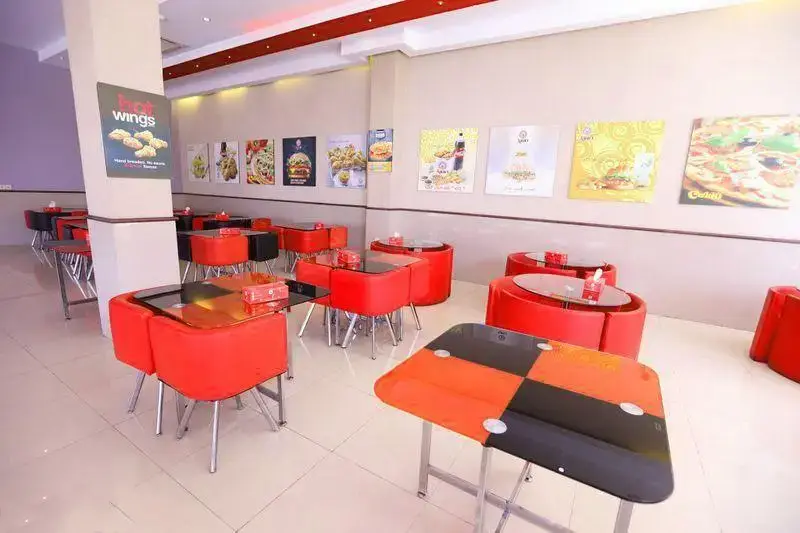 محیط دلنشین و دکوراسیون مدرن فست فود آریو، شامل میز و صندلی‌های شیک قرمز و مشکی و تصاویر متنوع غذاها روی دیوار.