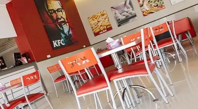 دکوراسیون داخلی فست فود آریو با تم رنگی قرمز و نارنجی، شامل میز و صندلی‌های شیک و لوگوها و پوسترهای مشهور KFC روی دیوارها.