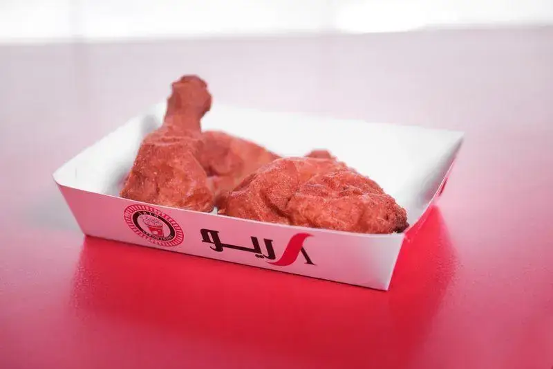 عکس از ران و سینه مرغ سوخاری اصیل و لذیذ فست فود آریو، با بسته بندی خاص این برند در پس‌زمینه قرمز.