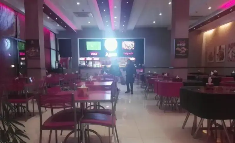 نمایی از فضای داخلی رستوران فست فود آریو با دکوراسیون مدرن، نورپردازی صورتی، میز و صندلی‌های شیک، و پیشخوان سفارش غذا و نوشیدنی.