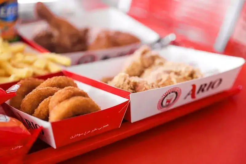 نمای نزدیک از سینی فست فود آریو شامل مرغ سوخاری ترد، ناگت مرغ و سیب زمینی سرخ کرده تازه روی میز قرمز رستوران.