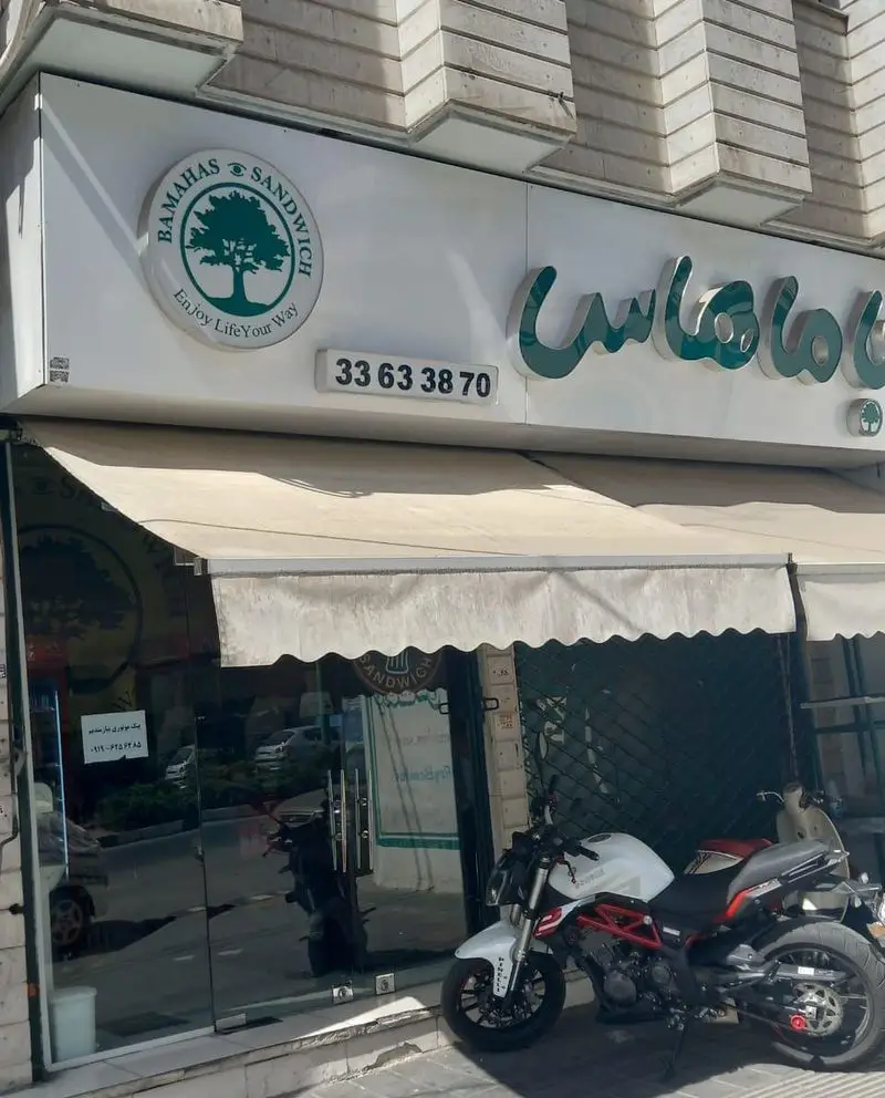 تصویر نمای بیرونی کسب و کار باماهاس ساندویچ در شهرری، شامل تابلوی روشن با لوگوی درخت، شعار Enjoy Life Your Way و شماره تماس.