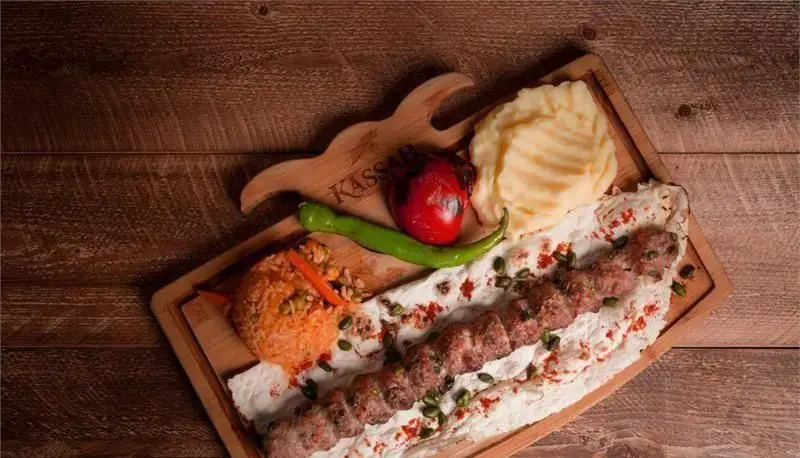 غذای اصلی رستوران کاساب: کباب سیخی گوشت با پوره، برنج، فلفل کبابی و نان محلی سرو شده روی تخته چوبی