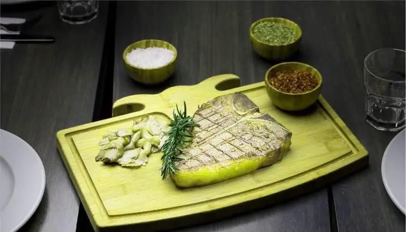 استیک تی-بون کبابی با رزماری و سیر تازه روی تخته چوبی، همراه با کاسه‌های نمک و ادویه. تجربه‌ای لذت‌بخش در رستوران کاساب.