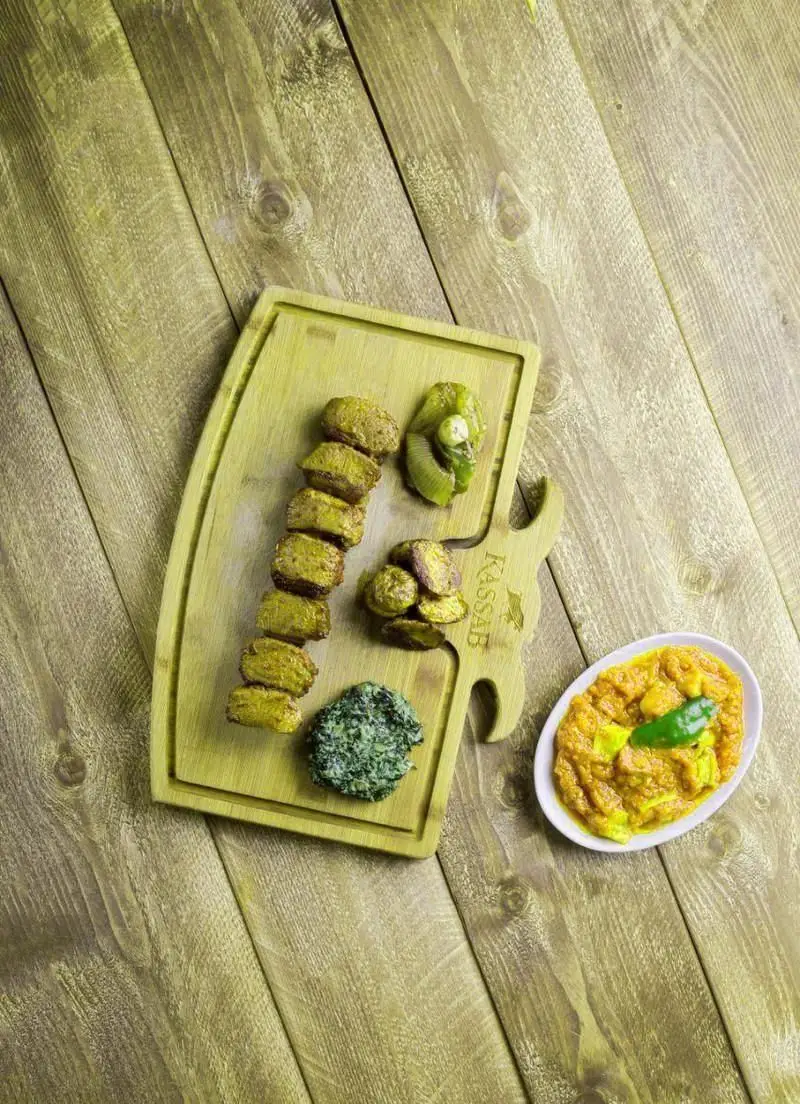 غذای خوشمزه و سالم از رستوران کاساب: سیب زمینی سرخ شده، سبزیجات شکم پر، دیپ اسفناج و خورشت لذیذ سرو شده بر روی دیس چوبی.