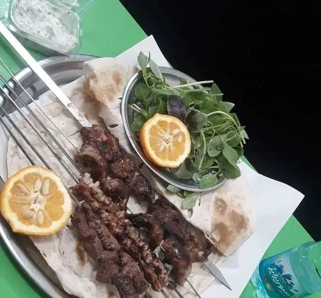 کباب‌های آبدار جگرسرای وحید شامل جگر، دل و قلوه روی نان داغ، همراه با سبزیجات تازه، لیمو و ماست. غذای سنتی ایرانی.