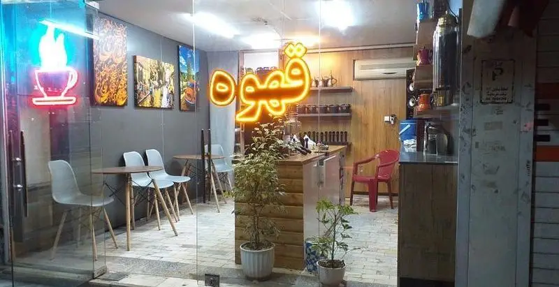 تصویر داخلی کافه قهوه موکا، یک کافه دنج با نورپردازی گرم، میز و صندلی مدرن، گیاهان سبز و تابلوهای هنری دیواری. مکانی عالی برای قهوه.