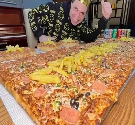 فست فود زنجیره ای پیانو: مردی خوشحال با تاج کنار بزرگترین پیتزا، سیب زمینی سرخ کرده و نوشیدنی های متنوع. لذت غذایی بی پایان.