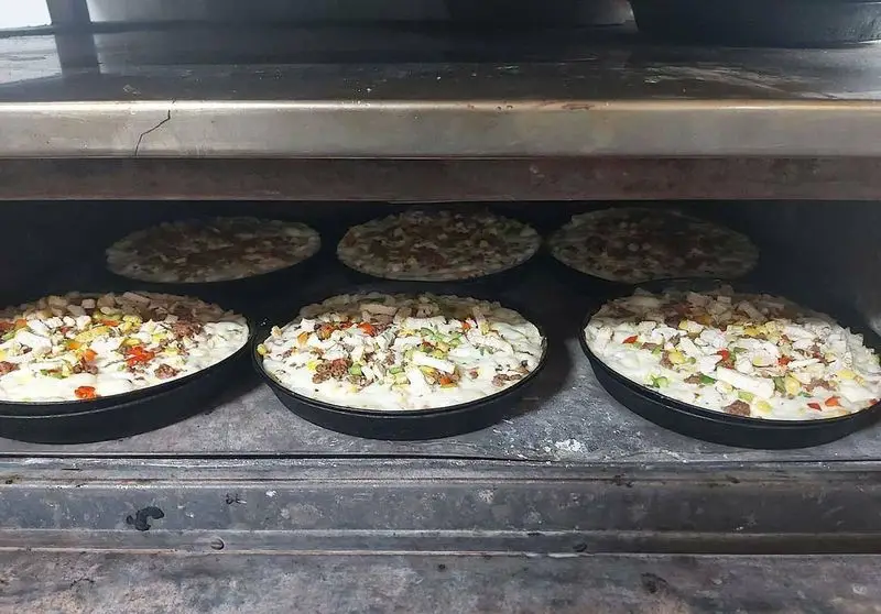 شش پیتزای تازه (دیپ دیش و معمولی) در حال پخت در فر فست فود زنجیره ای پیانو، تضمین طعم عالی و کیفیت بی‌نظیر.
