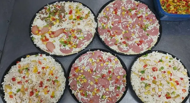 تصویری از چندین پیتزای خام تازه و با کیفیت فست فود زنجیره ای پیانو با تاپینگ‌های متنوع گوشت، سوسیس، مرغ و سبزیجات رنگارنگ آماده پخت.