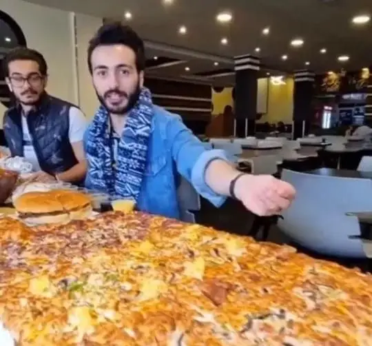 مردانی در فست فود زنجیره ای پیانو در حال نمایش پیتزا و همبرگرهای بزرگ. تجربه هیجان انگیز غذایی در رستوران پیانو.